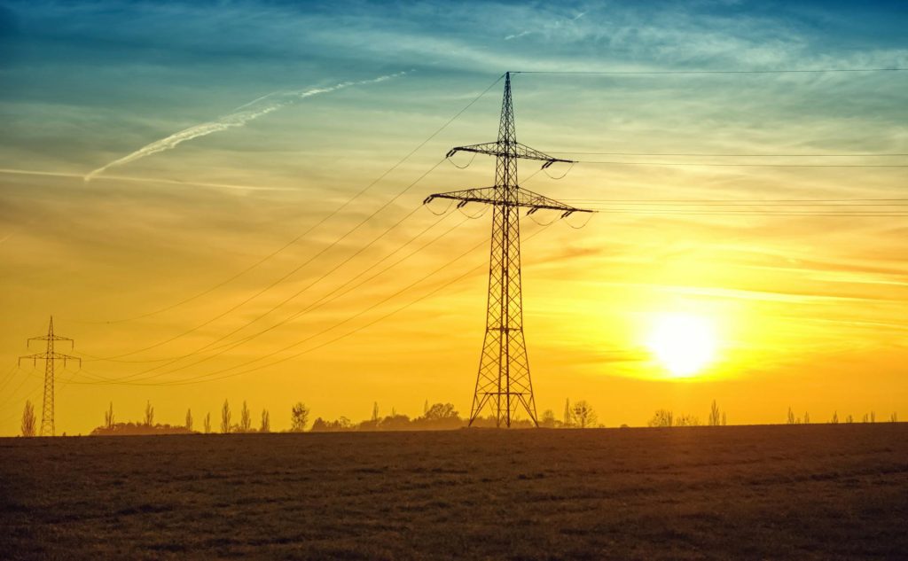 High-voltage electricity transmission tower at sunset representing energy infrastructure economic impact analysis